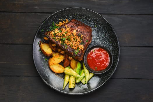 Top view of juicy grilled pork ribs with potato wedges and cucumber