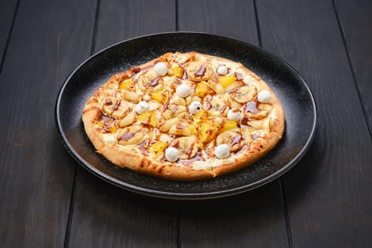 Sweet pie with banana, orange, cranberry in powdered sugar and caramel syrup