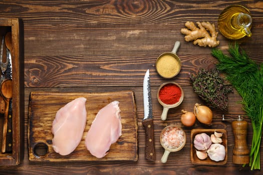 Culinary concept. Wooden background with chicken fillet, spices, herbs and utensil. Free space for text or recipe
