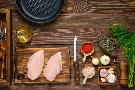 Culinary concept. Top view of kitchen table with chicken fillet, aromatic herbs and spices for cooking and utensil.