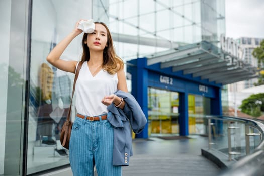 Asian beautiful business woman drying sweat her face with cloth in warm summer day hot weather, Female having sunstroke skin damage from sun UV city air pollution outdoors on street