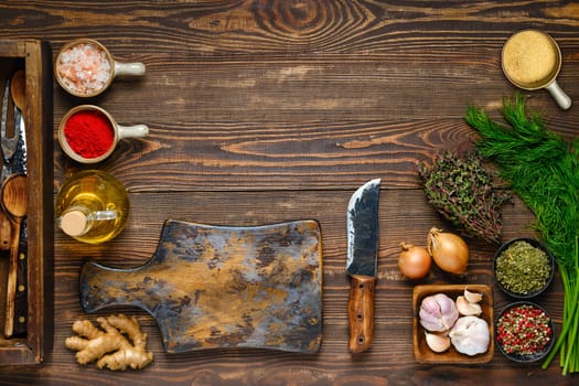 Culinary concept. Top view of wooden kitchen table with empty cutting board, spice, herbs and utensil. Free space for text or recipe.