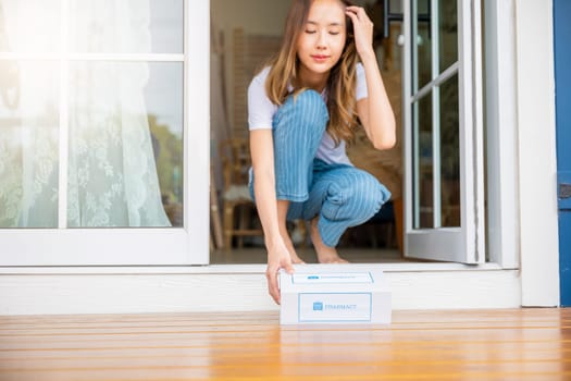 Close up hands of sick Asian woman sitting at door to receive medication first aid pharmacy box from hospital delivery service at floor home, female patient buy drugstore online business, healthcare
