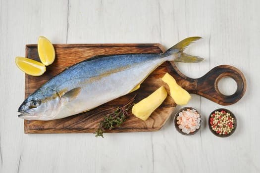 Top view of whole fresh chinook on wooden cutting board with spice, lemon and ginger
