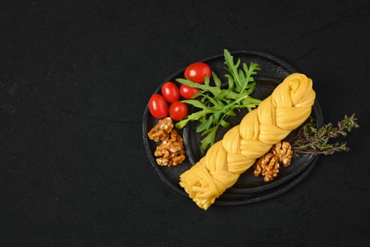 Smoked braided cheese with walnuts and tomatoes on a plate, top view