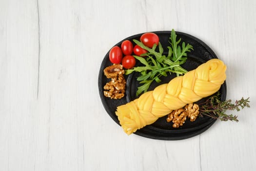 Smoked braided cheese with walnuts and tomatoes on a plate, top view