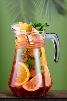 Pitcher with cold citrus sangria over green background