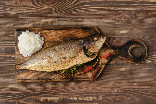 Yellow tailed mackerel with rice baked in oven on wooden cutting board, top view