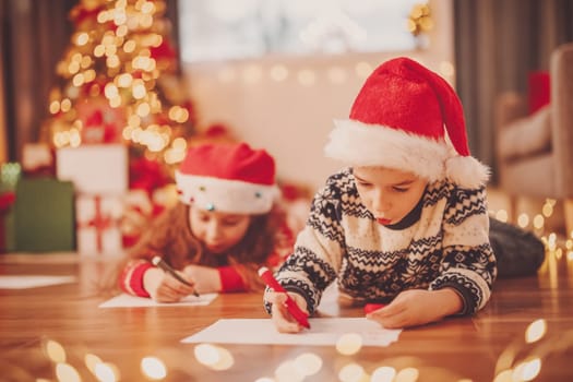 Children lying on the floor indoors and writing letters for Santa Claus. Concept of the Christmas eve.