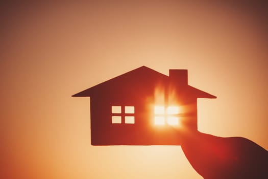 Woman's hand holding a model of a house on sunset evening. Concept of buying or selling a new appartment.