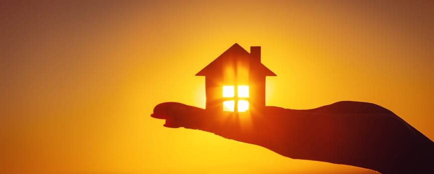Woman's hand holding a model of a house on sunset evening. Concept of buying or selling a new appartment.