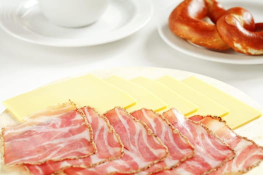 Ham and cheese on wood plate with bread roll and cup