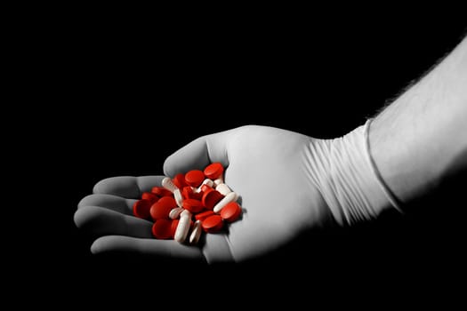 hand with medical glove holding pills over black background
