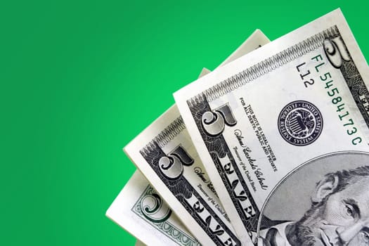 Closeup of five dollar bills against green gradient background.