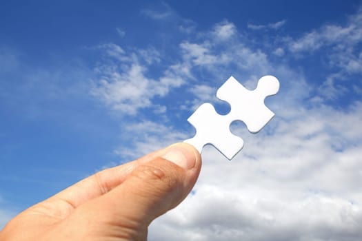 Hand with jigsaw piece instead of key and blue sky background