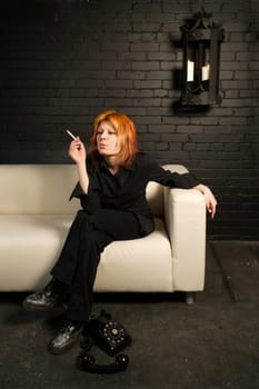 Female with dyed orange hair sitting on a couch smoking a cigarette.