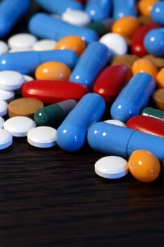 Collection of assorted pills on a dark wood table. Shallow depth-of-field.