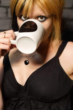 Female drinking coffee against the black brick wall of a urban café.