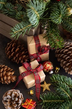 Wrapped gift boxes between Christmas decorations, pine cones and green fir branches top view on dark black background. Christmas or New Year Holiday atmosphere flat lay
