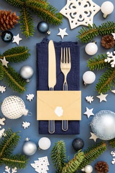 Blue and white Christmas table setting with envelope near decorations and fir tree branches top view. Winter table with fork, knife and plate. Winter New Year or Christmas dinner atmosphere