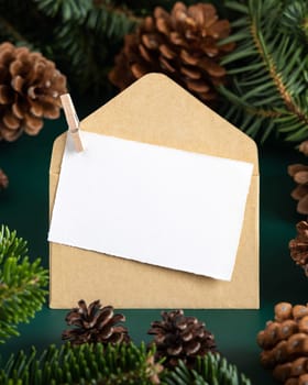 Blank card and envelope between fir branches and pine cones on green close up, mockup. Christmas or New Year greeting card template, Holiday winter composition