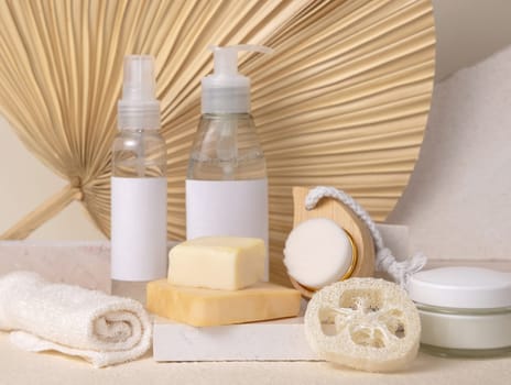 Small bottles and handmade soap bars on stone against dry beige palm leaf close up, label mockup. Skincare beauty products, cream or lotion. Natural organic cosmetics. Minimal eco friendly composition..
