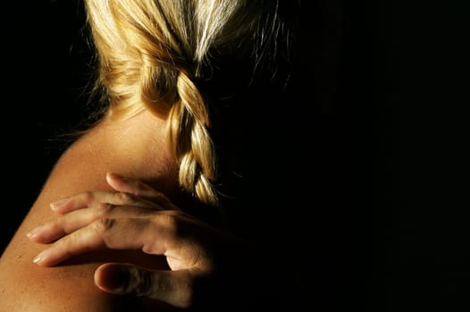Abstract dramatically lit image of woman's shoulder, hand and blond hair on a black background.
