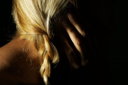 Abstract dramatically lit image of woman's shoulder, hand and blond hair on a black background.