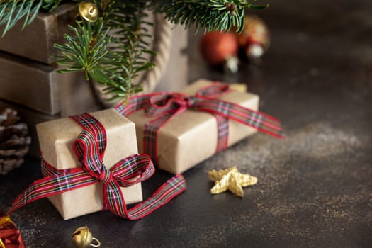 Wrapped gift boxes between Christmas decorations, pine cones and green fir branches close up on dark background, copy space. Christmas or New Year Holiday atmosphere flat lay