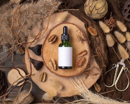 Green glass dropper bottle on wood near natural boho decorations top view, cosmetic packaging mockup. Skincare beauty product, serum or essence. Bohemian eco friendly flat lay with dried leaves.