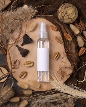 Transparent Refillable spray bottle on wood near natural boho decorations top view, label mockup. Skincare beauty product, lotion or essence. Bohemian eco friendly cosmetics flat lay with dried leaves.