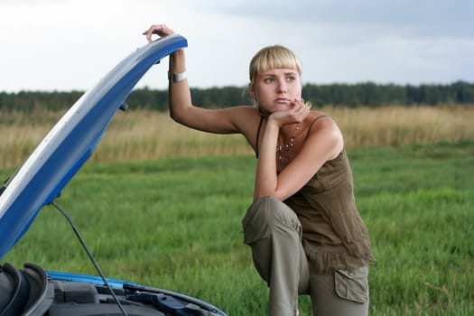 young blond woman with her broken car. The girl is sad