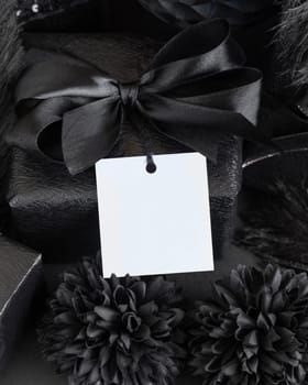Wrapped Gift Boxes with black paper flowers and decorations and square gift tag, mockup, copy space. Dark composition with blank label card for Birthday, Anniversary or black party present
