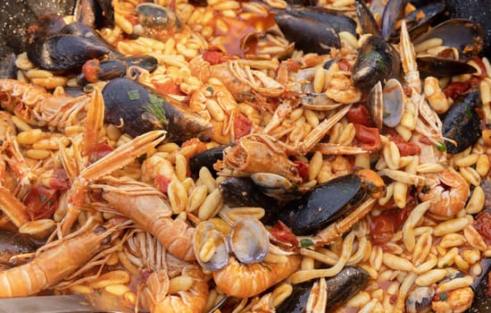 Italian Cavatelli allo scoglio, pasta with seafood and tomatoes close up in a frying pan. Mediterranean Apulian traditional food with fresh stewed clams, shrimps, mussels, octopus and squid
