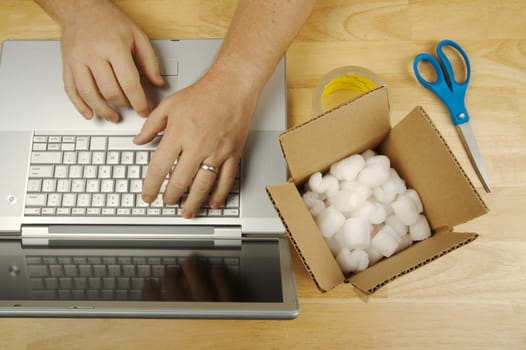Businessman Works on Laptop with sales item and packaging materials at his side.