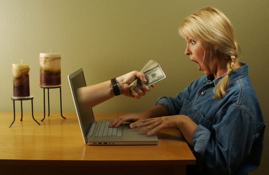 Attractive business woman shocked to see a hand coming through her laptop screen handing her lots of money. Can it be that simple? Gambling? Online business? Stock market? Your choice.