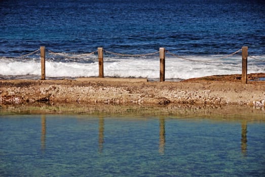 Reflections in ocean pool by coast with blue sea