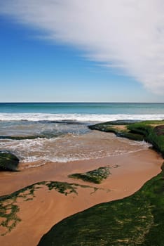 Sandy beach with blue ocean and blue sky and moss covered rocks