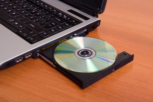 Partial view of a laptop with the dvd recorder opened on a wood table