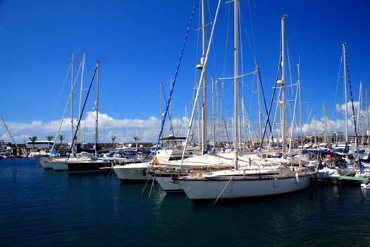 A marina with large yachts in the foreground and a deep blue sky background