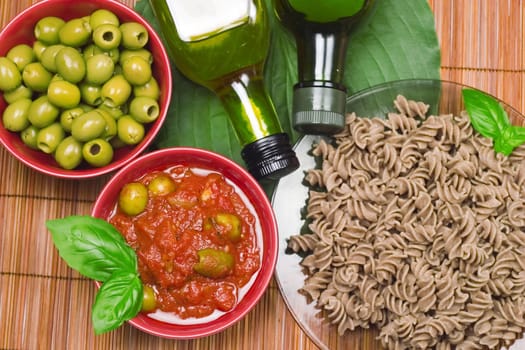 Delicious dinner: pasta, tomato sauce, olives and two olives oil bottles.