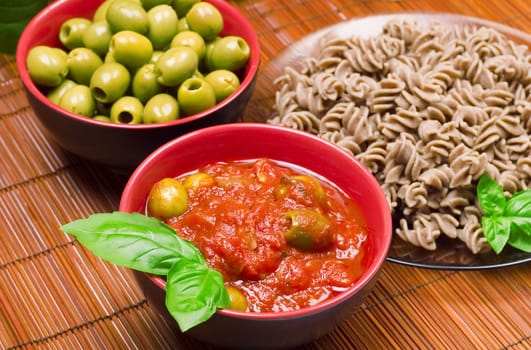 Delicious dinner: pasta, tomato sauce, olives and two olives oil bottles.