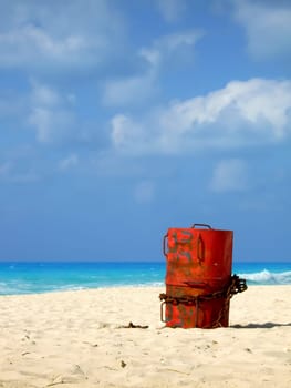 A red barrel with a chain around it standing still on the beach.