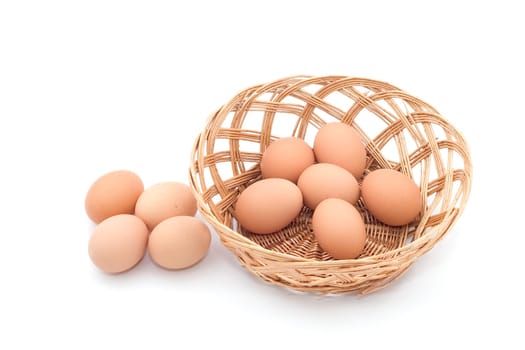 A whicker basket with eggs inside, there are more eggs outside the basket.