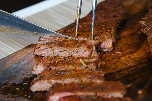 Cutting juicy grilled top blade beefsteak on wooden cutting board (photo with shallow depth of field)