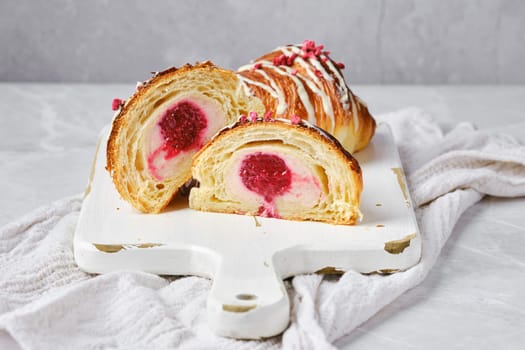 Croissant cut in half, showing the cross section with raspberry stuffing on white serving board