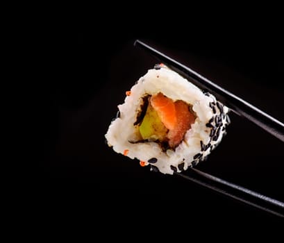 Closeup of traditional japanese sushi roll with salmon and tuna fish on bamboo chop sticks over black background. Sushi bar menu design with copyspace.