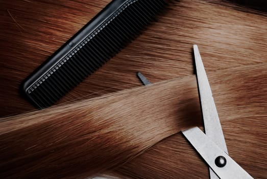 Healthy long brown dyed hair lock extensions and professional hairdresser scissors and comb. Hairstyle and hair treatment salon accessories.