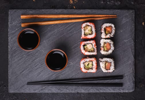 Top view of traditional japanese cuisine. Sushi rolls with salmon and tuna fish on black sushi board from above.