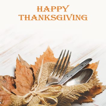 Thanksgiving dinner table setting with autumn leaves and vintage silverware. Thanksgiving holiday design with seasonal table arrangement.